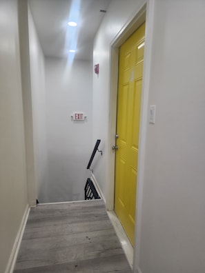 A stairway with a yellow door at the end, an exit sign, and a handrail. - Fantastic 2-bedroom apartment with AC in Drexel Hill (Drexel Hill)