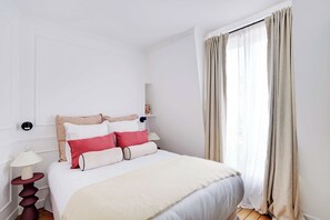 Ein Schlafzimmer mit einem Bett, einem Nachttisch, einer Lampe und einem Fenster mit Vorhängen.