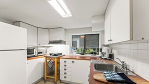 Moderni keittiö, jossa on valkoiset kaapit, puinen työtaso, sisäänrakennettu uuni ja ikkuna, josta avautuu näkymä vehreään maisemaan.