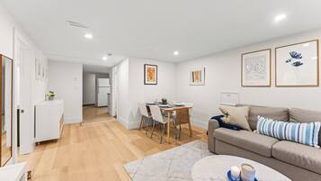 A modern living room with a sofa, a dining table, and a kitchen area in the background.