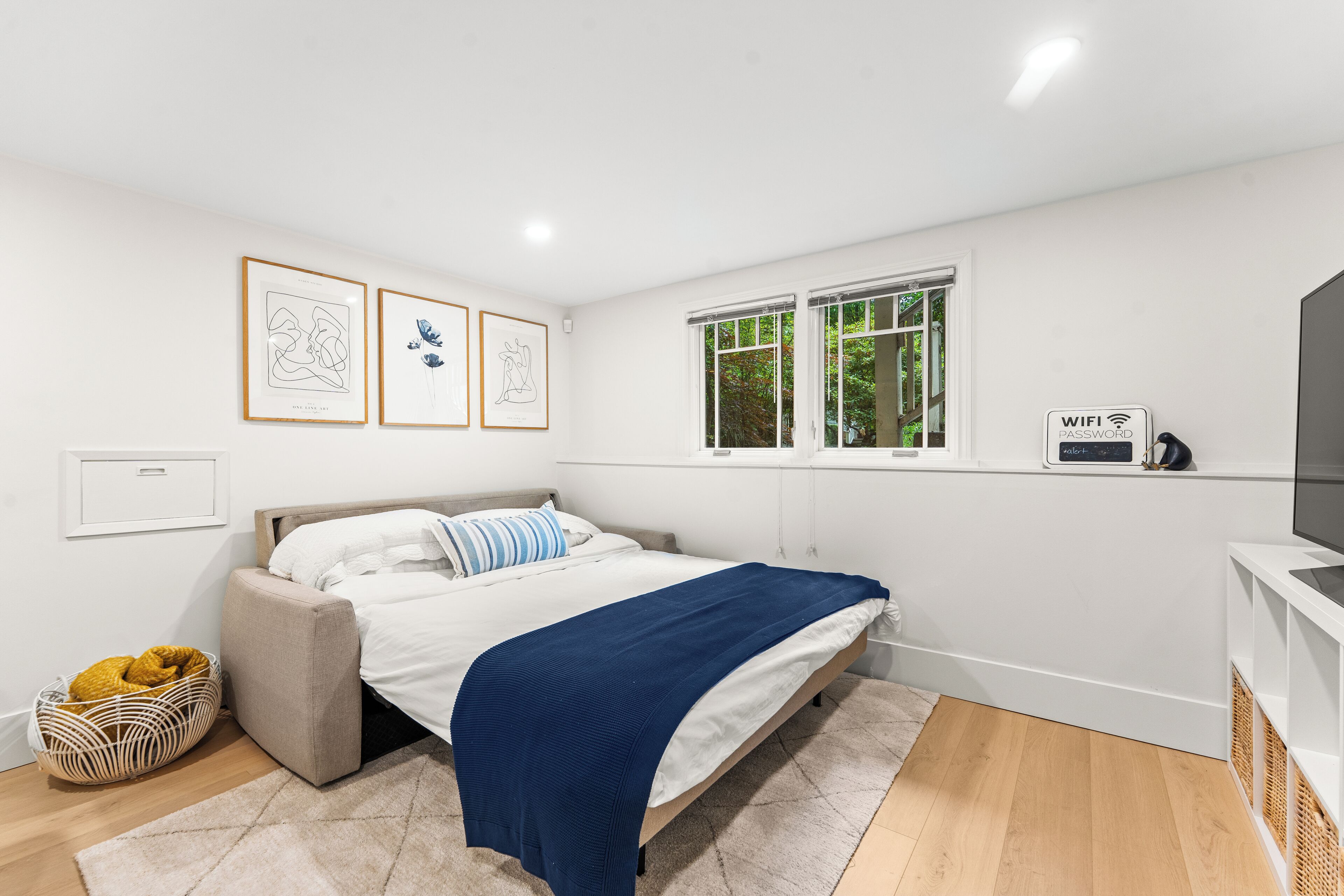 A bedroom with a bed, a window, a wall-mounted WiFi sign, and framed artwork.