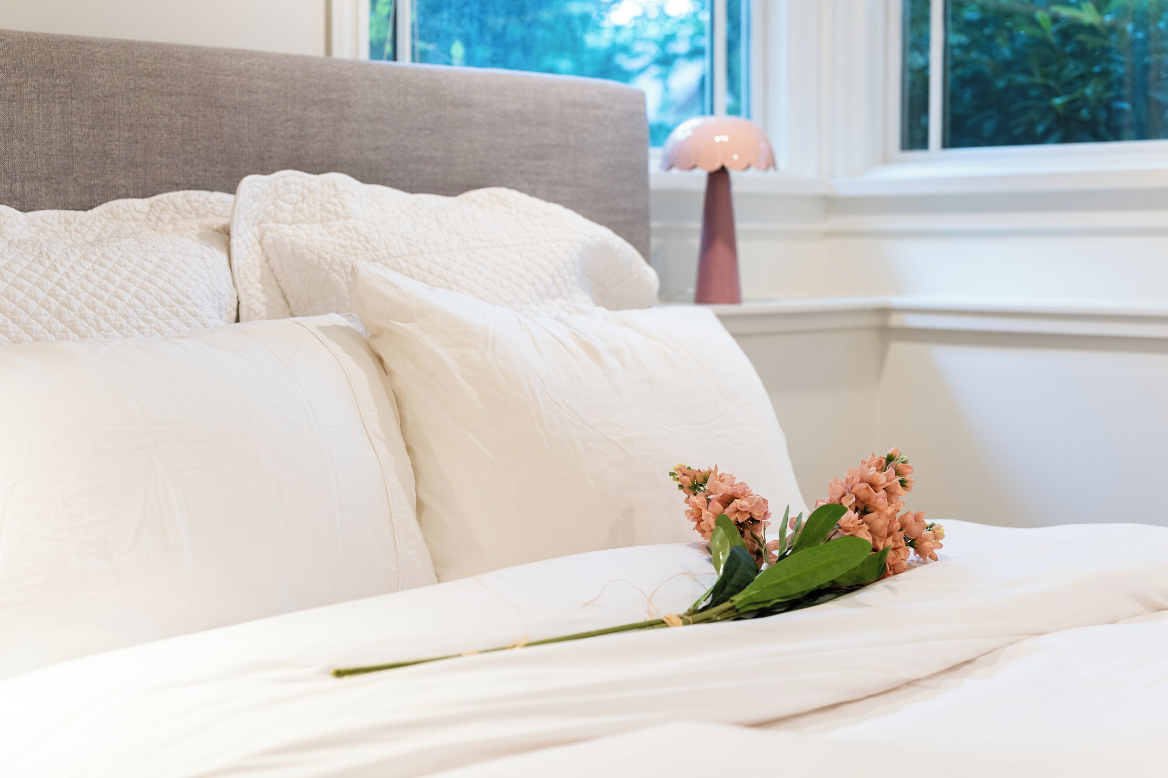 Ein ordentlich bezogenes Bett mit weißen Leinen und einem Blumenstrauß darauf.