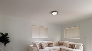 A modern living room with a sectional sofa, a coffee table, a potted plant, and a large window with blinds. - Modern Home • Walk to Design Dist• Free Parking (Miami)