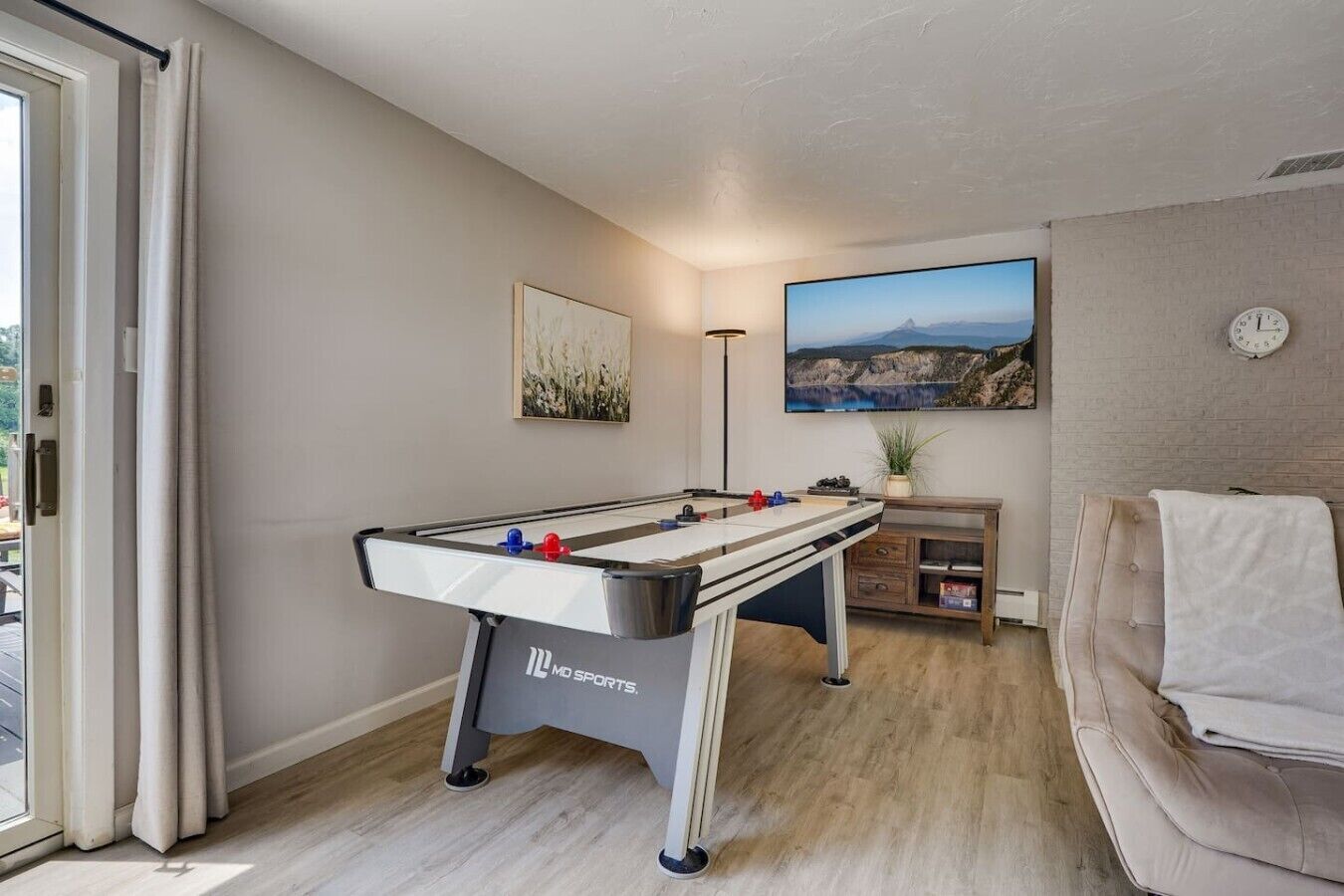 A room with a foosball table, a sofa, a painting, a clock, and a window.
