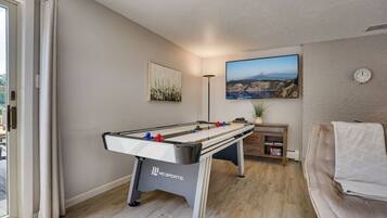 A room with a foosball table, a sofa, a painting, a clock, and a window.
