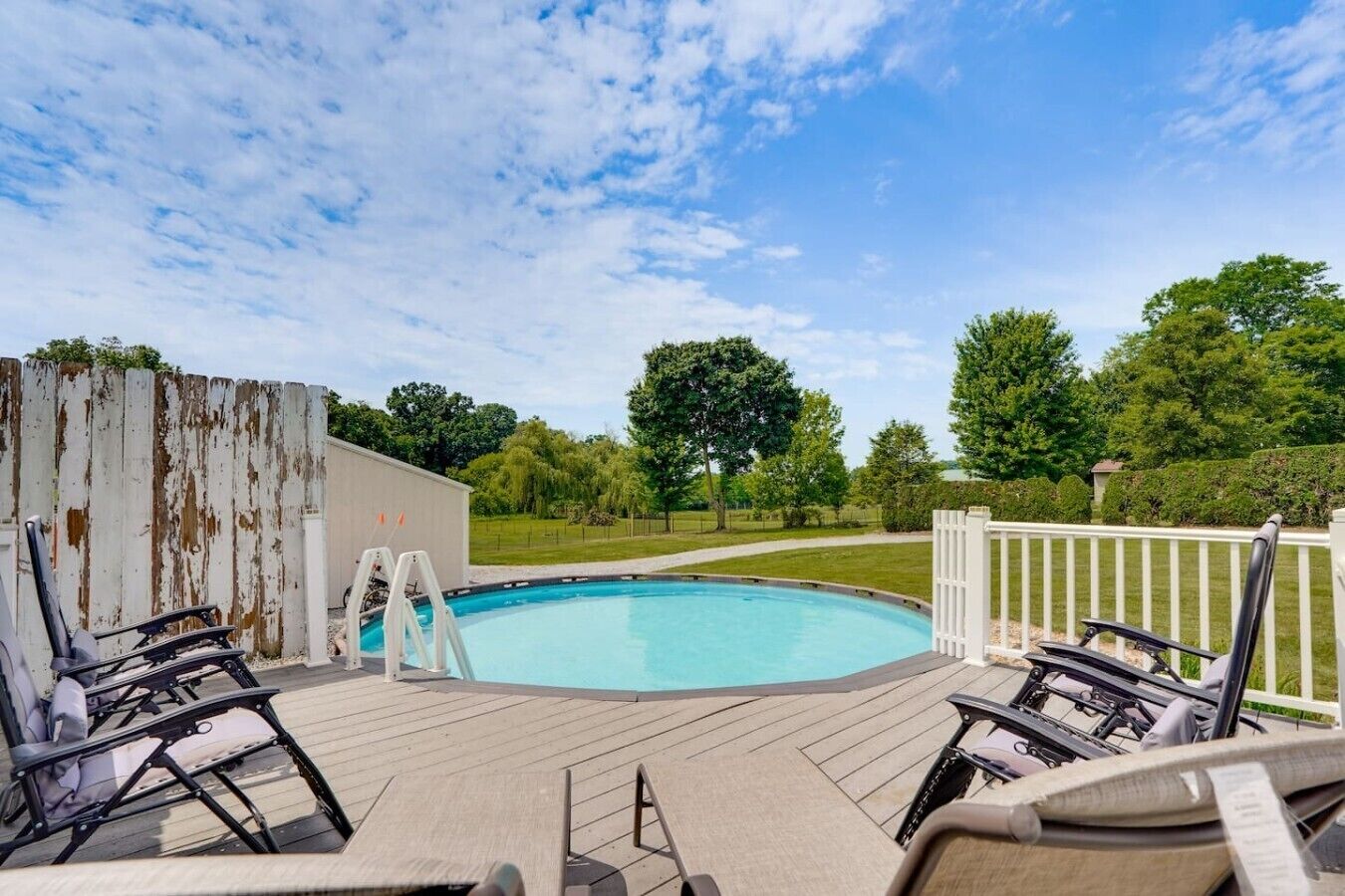 Ein Swimmingpool mit Holzterrasse, weißem Zaun und Liegestühlen.