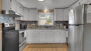A kitchen with white cabinets, a stainless steel refrigerator, a built-in oven, and a window with blinds.