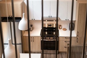 A kitchen with wooden cabinets, a stainless steel stove, and a white pendant light. - Spa, Comfort & Escape | ASKA (Saint-Côme)