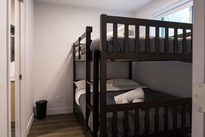 Ein Etagenbett mit Fenster darüber, eine Tür links und eine Mülltonne in der Ecke.
