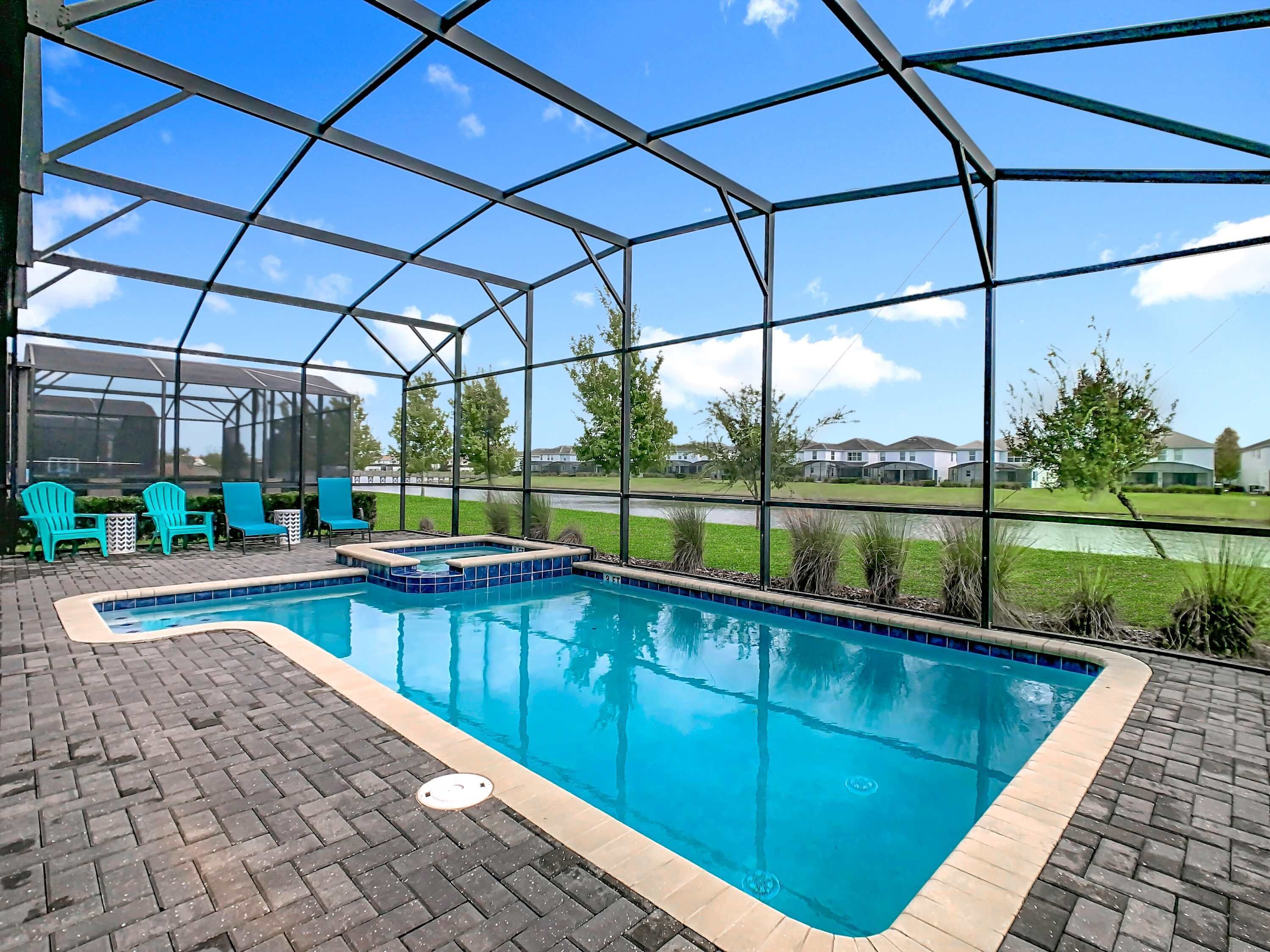 A covered outdoor swimming pool with blue tiles, surrounded by a brick patio, and a view of houses in the background.