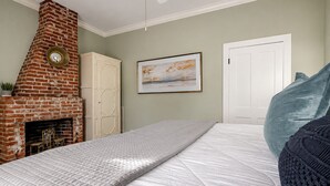 Un dormitorio con chimenea de ladrillo, una cama con colcha acolchada, un cuadro enmarcado en la pared y una puerta blanca.