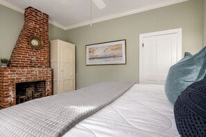 Ein Schlafzimmer mit Kamin aus Ziegelsteinen, einem Bett mit gesteppter Bettdecke, einem gerahmten Gemälde an der Wand und einer weißen Tür.