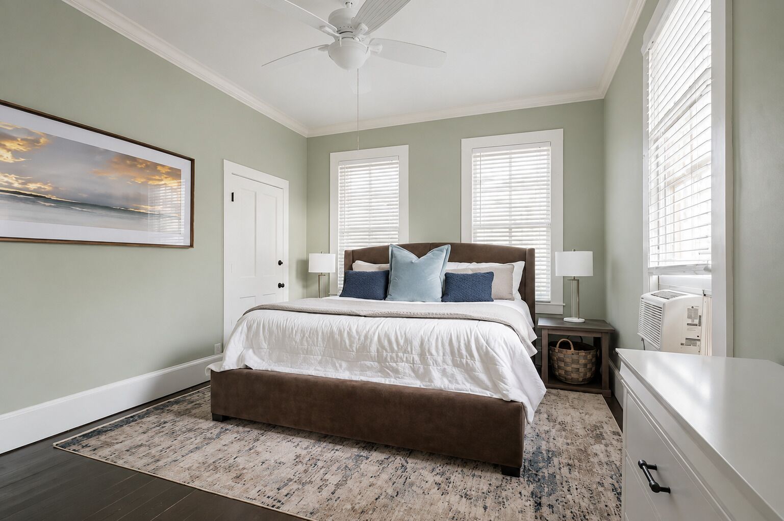A bedroom with a bed, a ceiling fan, a nightstand, a lamp, and a window with blinds.