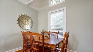 Un comedor con una mesa y sillas de madera, un espejo decorativo en la pared y una ventana con persianas.