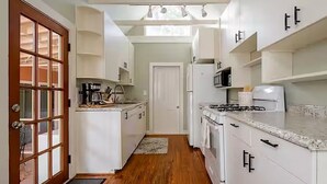 Una cocina con armarios blancos, piso de madera y una puerta que da a un pasillo.