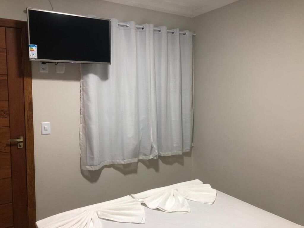 A room with a bed, a television mounted on the wall, and a curtain.