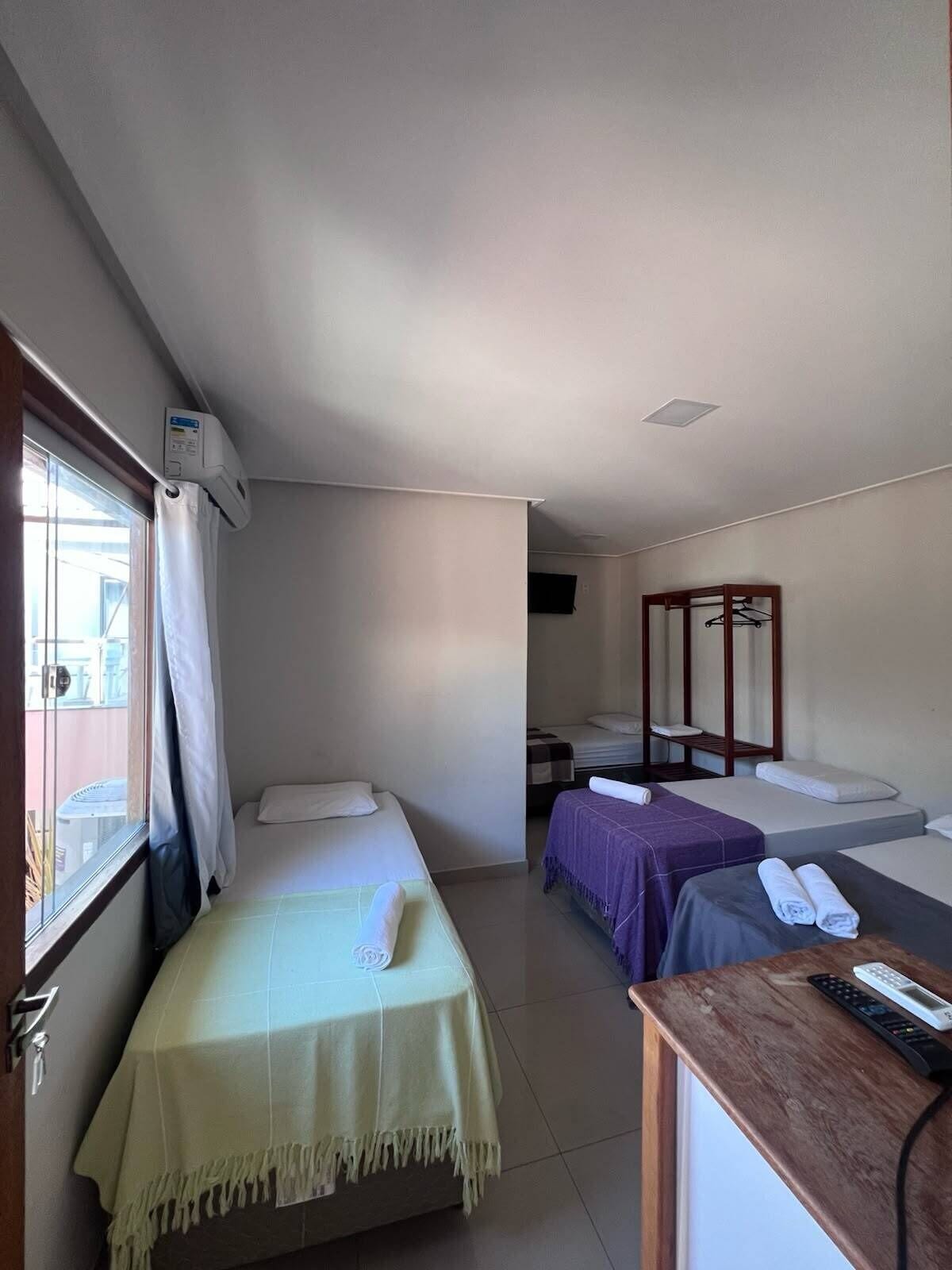 Habitación de hotel con dos camas individuales, una mesa de madera y un control remoto, y una ventana con cortinas.