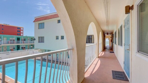 A corridor with a pool on one side and a building with balconies on the other. - Rooftop Oceanview Condo on the Beach Sand w/ Pool! (North Redington Beach)