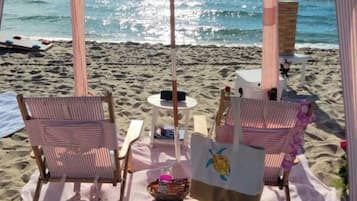Ein Sitzbereich am Strand mit gestreiften Stühlen, einem Tisch und einem Sonnenschirm.