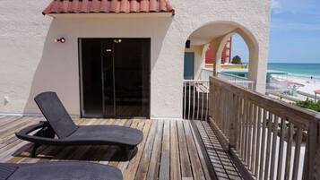 A balcony with a wooden deck, a black lounge chair, and a view of the beach.