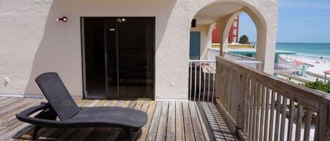 A balcony with a wooden deck, a black lounge chair, and a view of the beach.