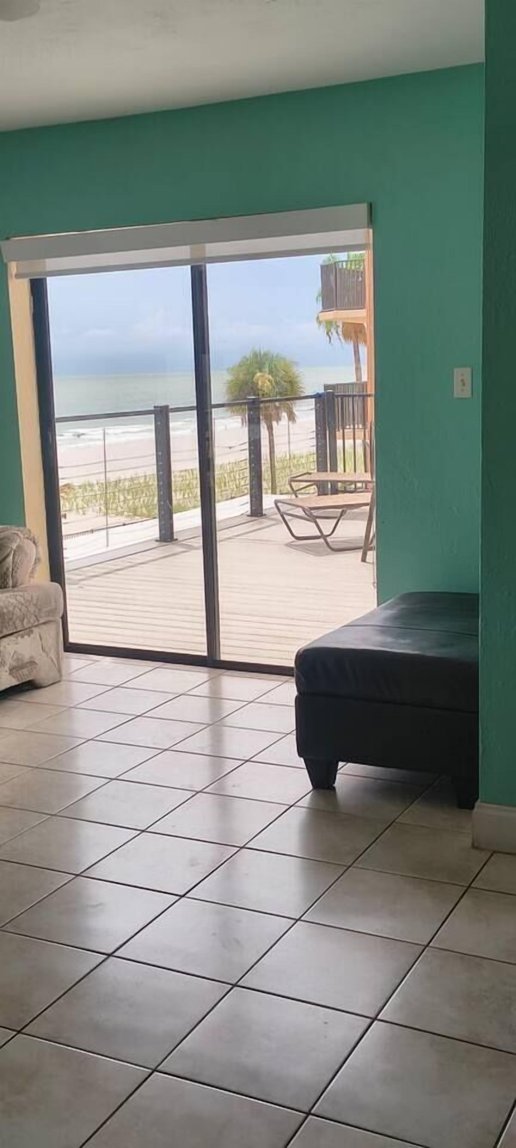 A room with a large sliding glass door leading to a balcony with a view of the beach.