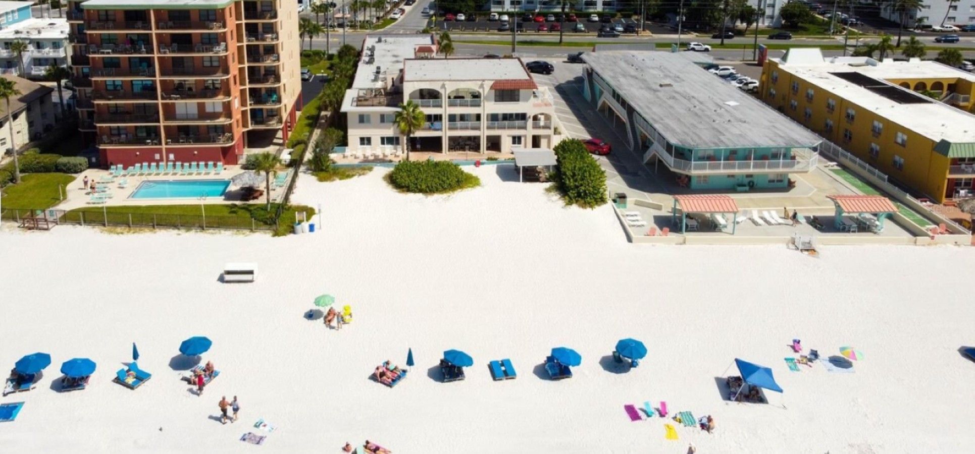 Una playa con tumbonas y sombrillas, una piscina y edificios al fondo.
