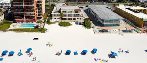 Una playa con tumbonas y sombrillas, una piscina y edificios al fondo.