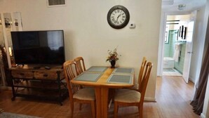 Zona pranzo con tavolo di legno, quattro sedie, televisore e orologio a parete.