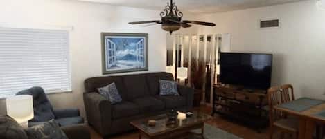 A living room with a sofa, a coffee table, a TV, and a ceiling fan.