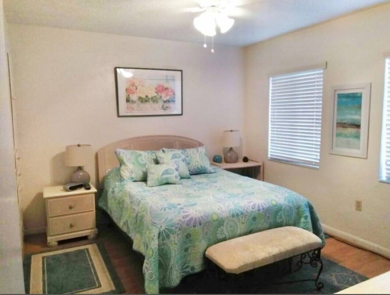 Une chambre à coucher comprenant un lit, des tables de chevet, un banc, un ventilateur de plafond et des œuvres d’art accrochées aux murs.