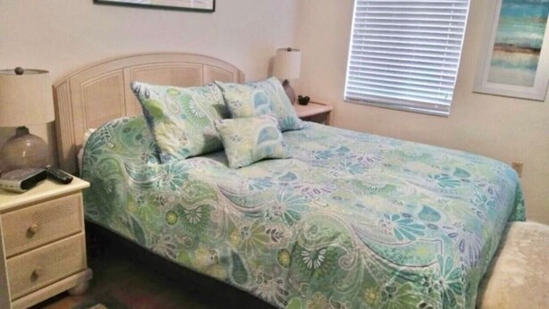 Una camera da letto con un letto, un comodino, una lampada e una finestra con persiane.