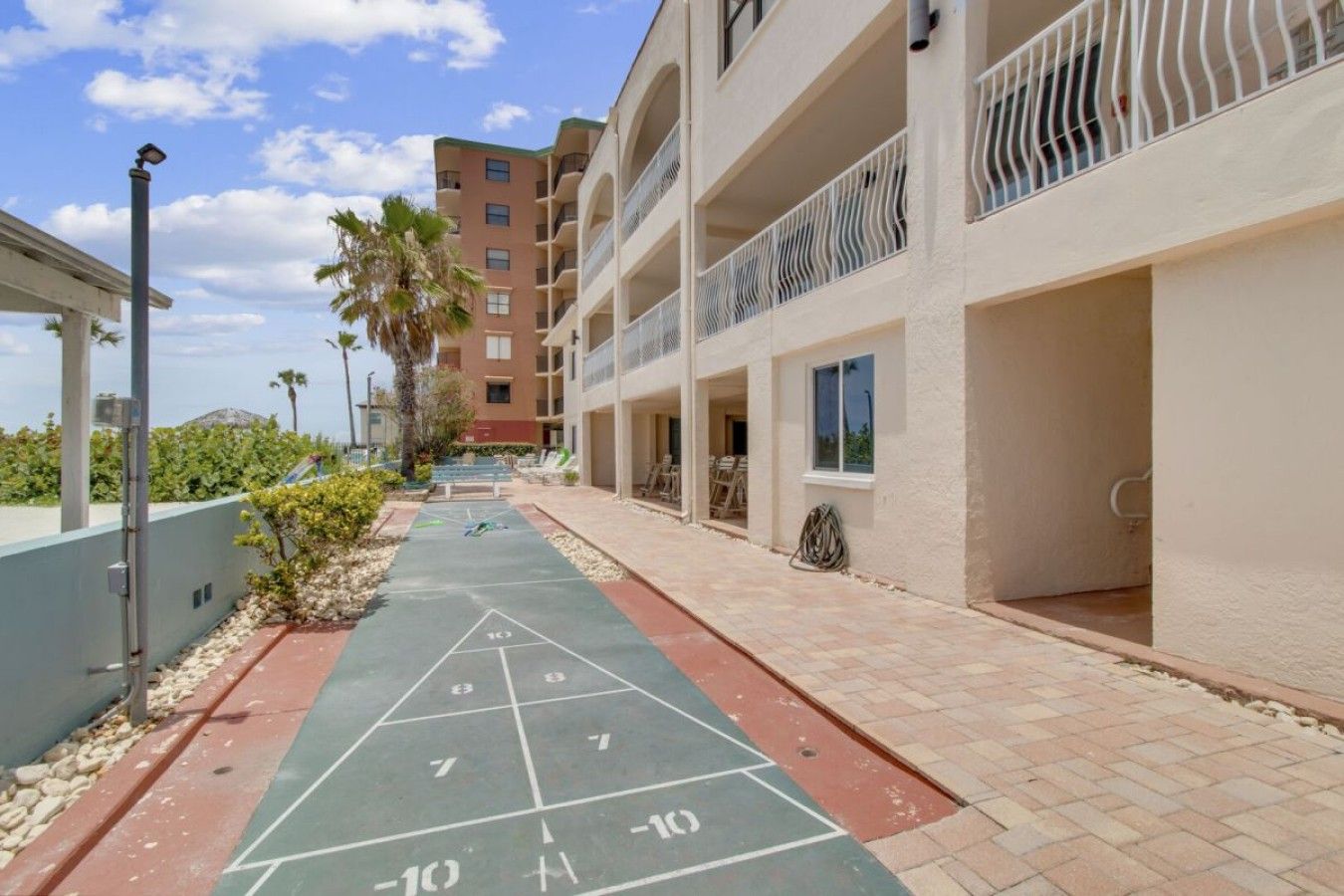 Un patio con cancha de juego de paletas, un edificio con balcones y una palmera.