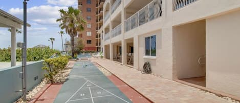 Un patio con cancha de juego de paletas, un edificio con balcones y una palmera.