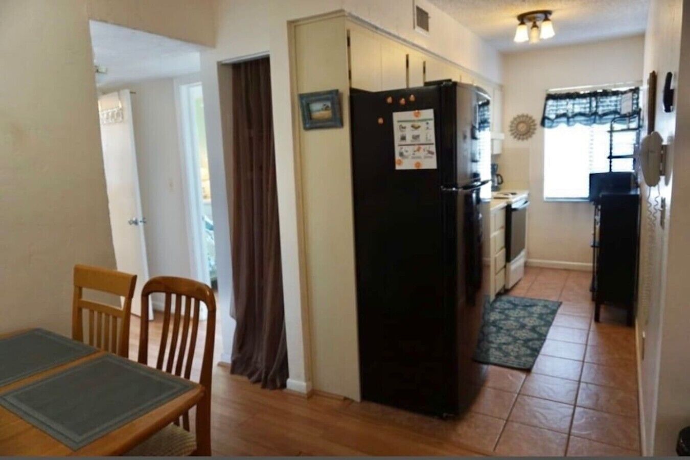 A compact kitchen with a refrigerator, a dining table with chairs, and a window with curtains.