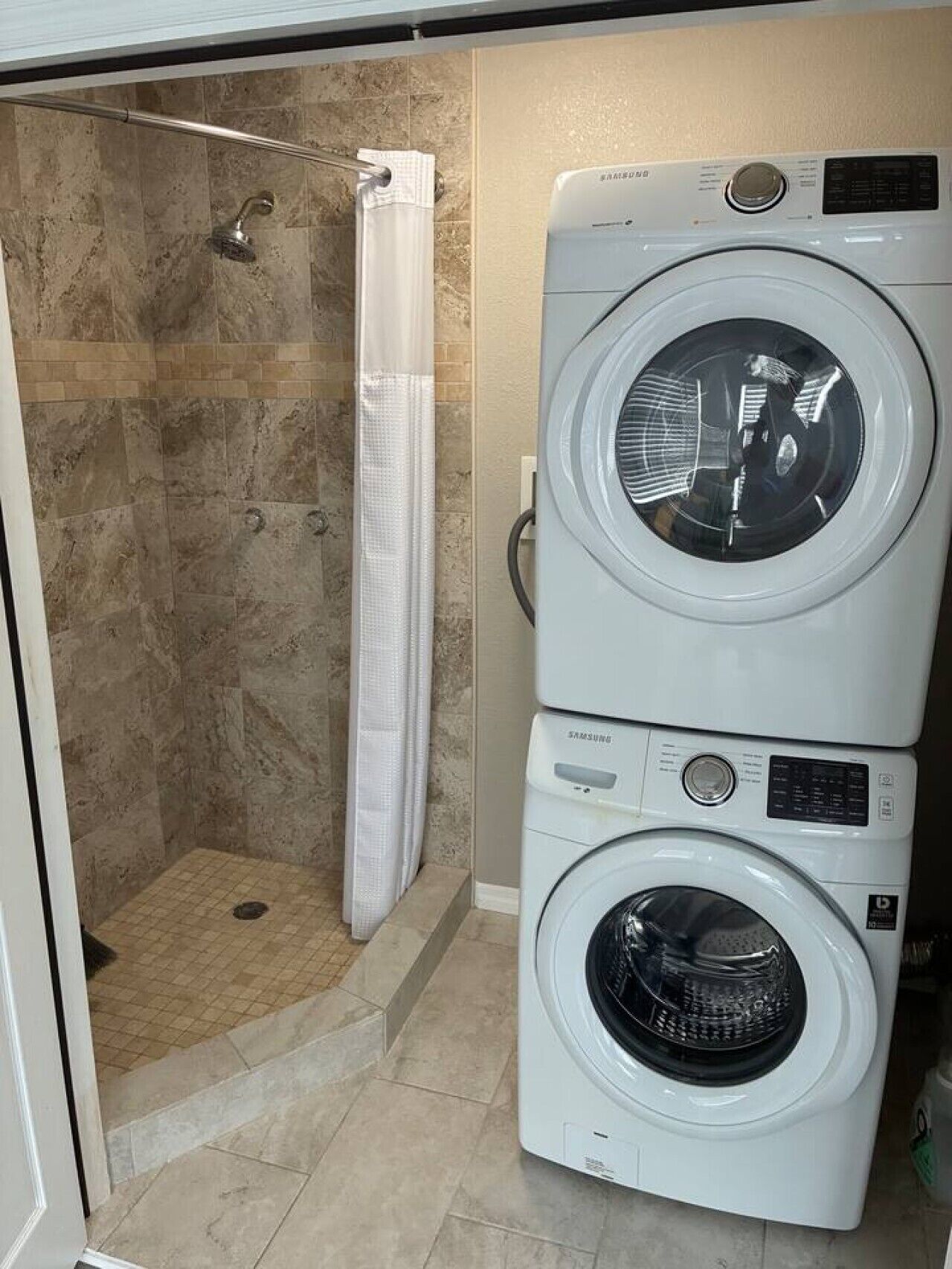 Un espace buanderie comprenant deux machines à laver superposées et un espace douche.