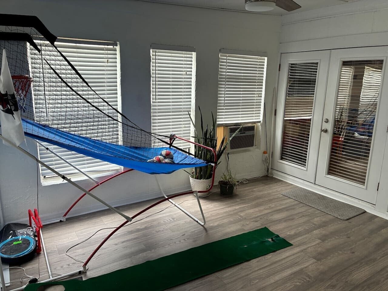 Una habitación con una hamaca, plantas en macetas y una puerta con ventanal.