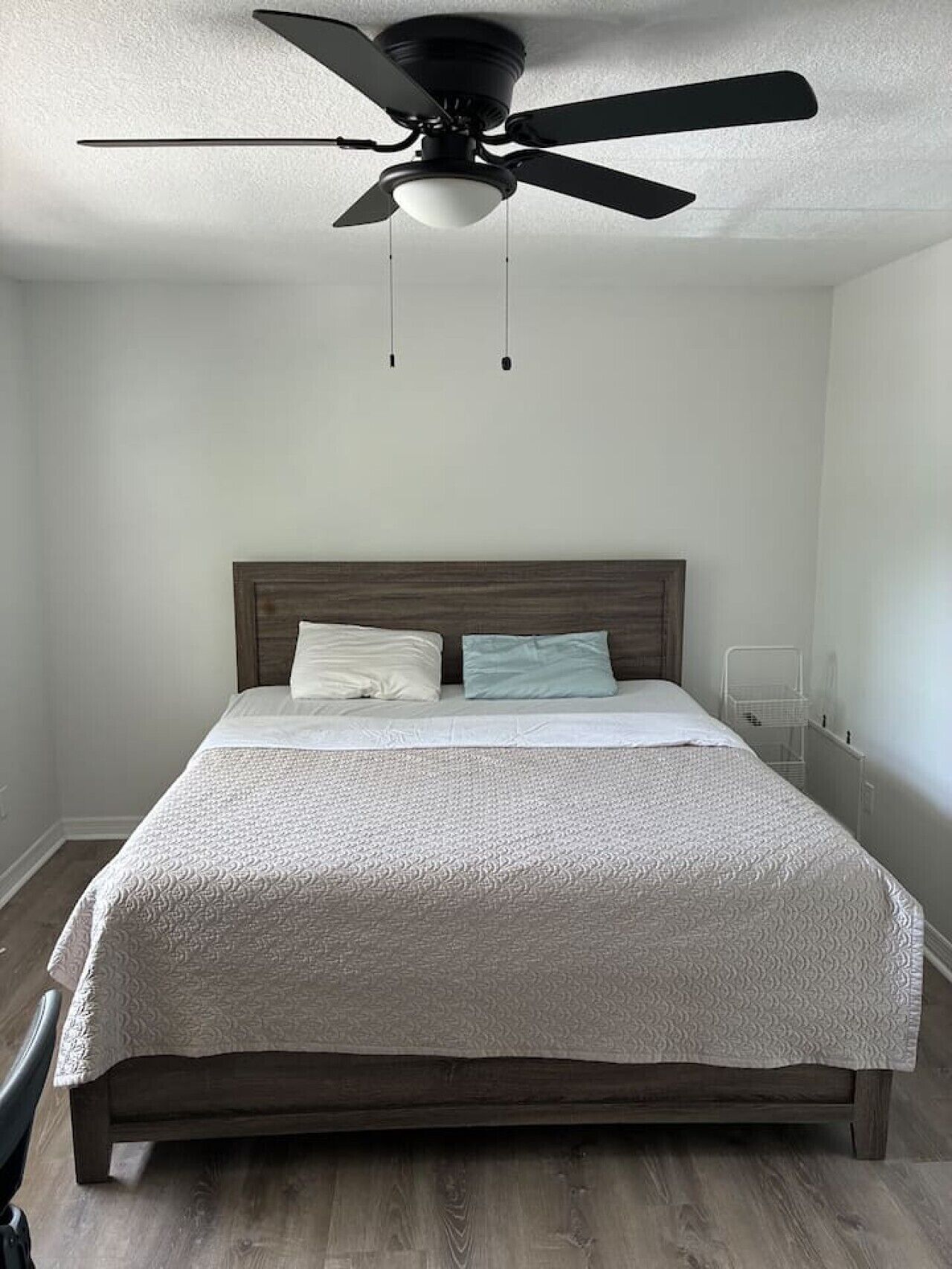 Ein Schlafzimmer mit einem Bett, einem Deckenventilator und einer weißen Wand.