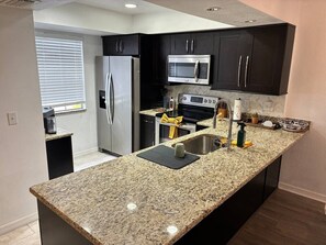 Una cocina moderna con encimeras de granito, electrodomésticos de acero inoxidable y armarios oscuros.