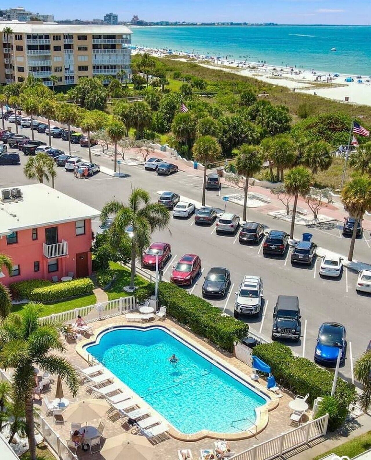 A hotel with a swimming pool, parking lot, and a view of the beach.