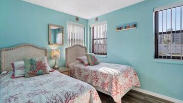Una habitación con dos camas, un espejo, una ventana con rejas y un estante pequeño.
