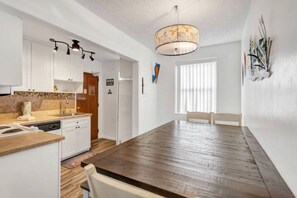 Una cocina moderna con gabinetes blancos, una encimera de madera y un lavavajillas integrado. Hay una zona de comedor con una mesa y sillas de madera.