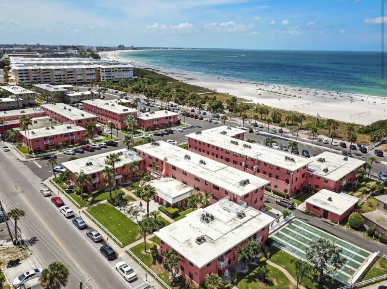 A coastal hotel with multiple buildings, a beach, and a road.