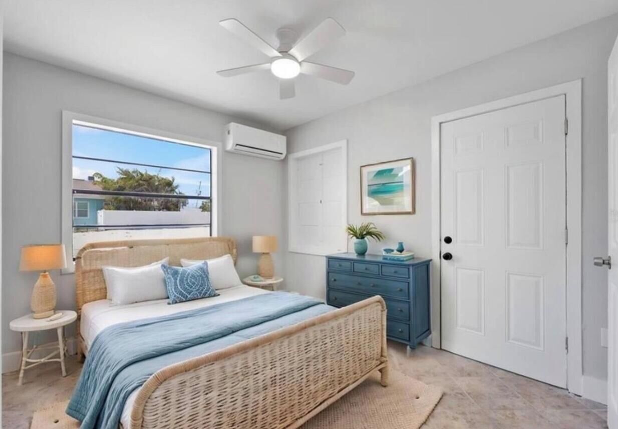 A bedroom with a bed, a ceiling fan, a window, a dresser, and a door.