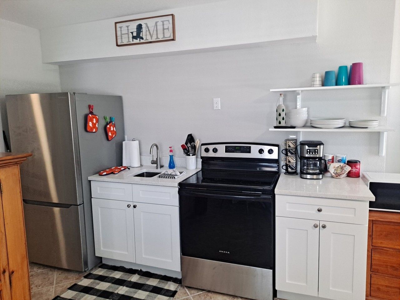 A compact kitchen with white cabinets, a stainless steel refrigerator, a black stove, and a coffee maker on the countertop.