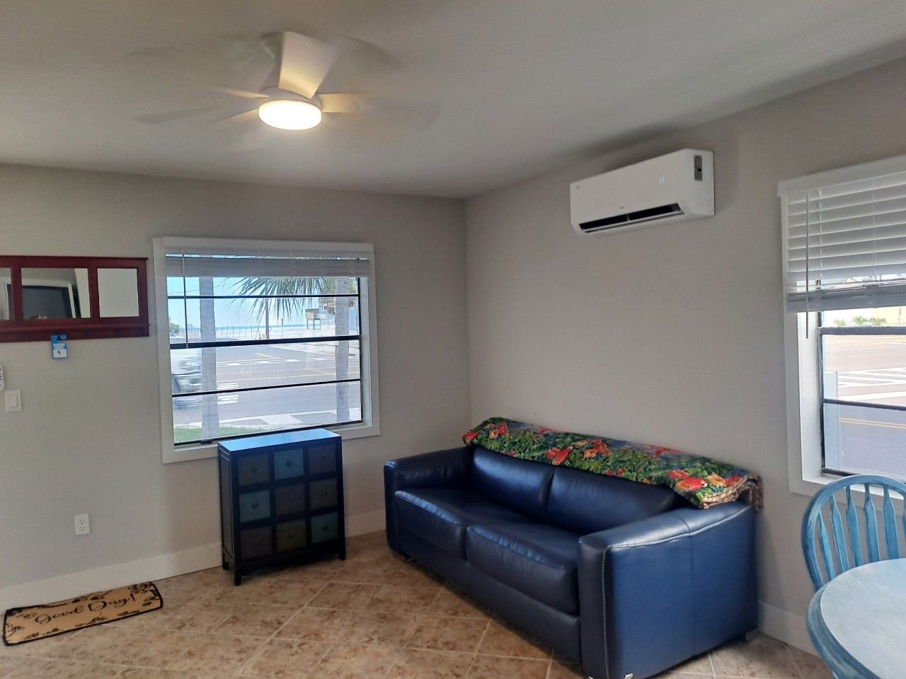 A room with a blue leather sofa, a small table, a ceiling fan, and an air conditioning unit.