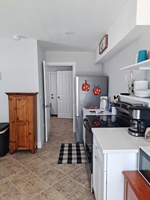 Cocina compacta con refrigerador, estufa y cafetera. Se observa también un mueble de madera y un tapete a cuadros blancos y negros.