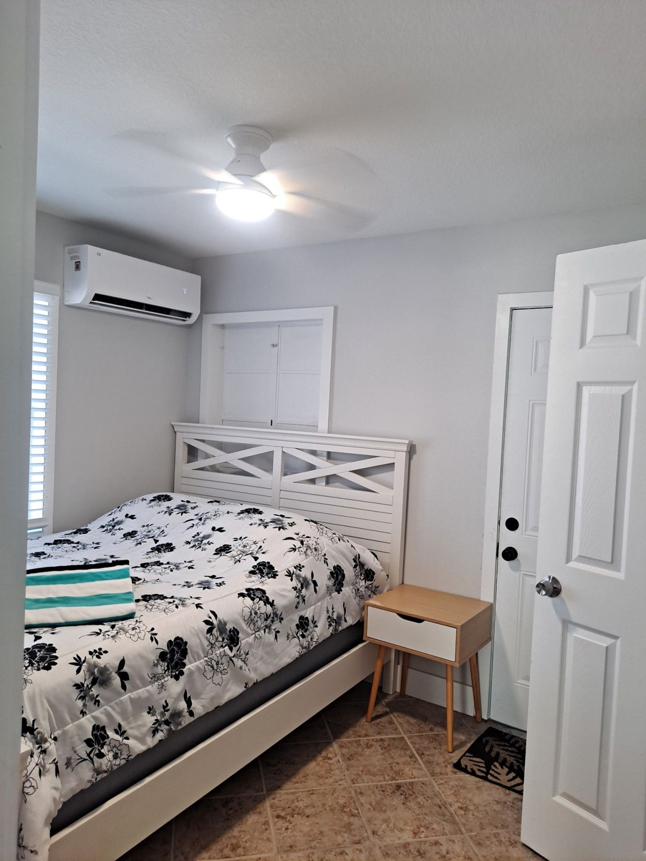 Quarto com cama, mesa de cabeceira, porta e aparelho de ar condicionado.