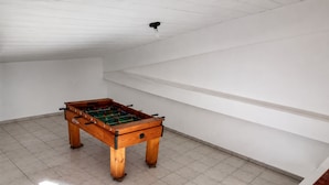 A room with a foosball table, white walls, and a sloped ceiling. - Casa Estrela Cond Fechado c Piscina - RJ (Cabo Frio)