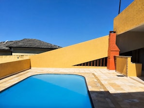 Ein Schwimmbecken mit klarer, blauer Wasseroberfläche, umgeben von einer gefliesten Terrasse und einer gelben Wand.
